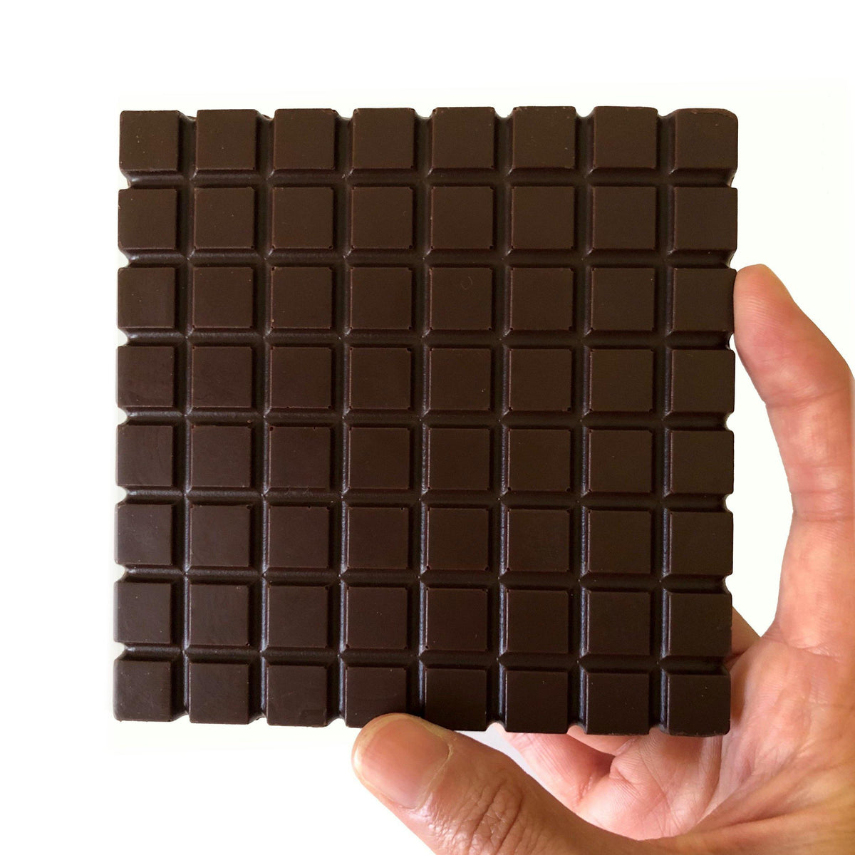 Hand holding a square bar of dark chocolate with uniform squares, showcasing rich cocoa texture.